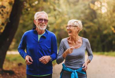 Smiling elderly couple jogging in a sunny park.