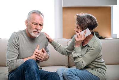 Man clutching chest, woman on phone, looking concerned.