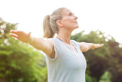 Woman stretching arms outside, looking upward, in a green park.