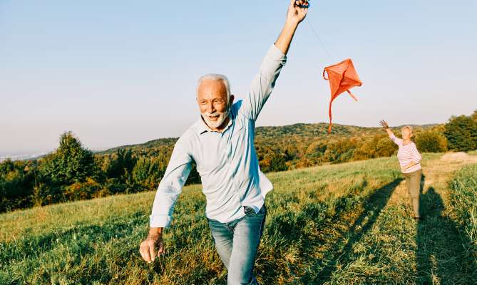 Happy middle-aged couple running and flying a red kite in an open field