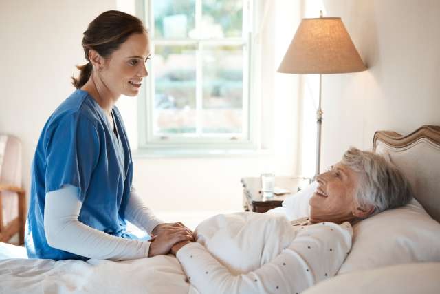 Nurse smiling at an elderly woman in bed.