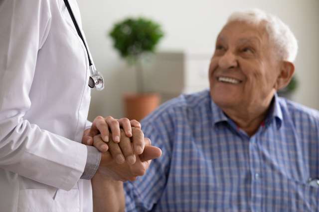 Doctor holding elderly man's hand, both smiling warmly.