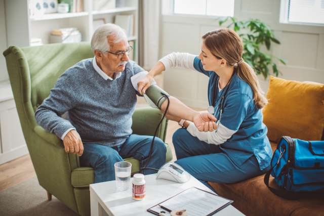 Nurse checking elderly man's blood pressure in a cozy living room.