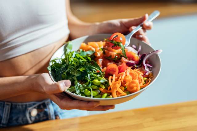 Person holding a colorful salad with greens and vegetables.