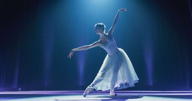 Ballet dancer performing on stage under blue light.