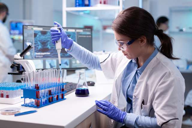 Scientist in a lab pipetting liquid into test tubes, focused and wearing protective gear.