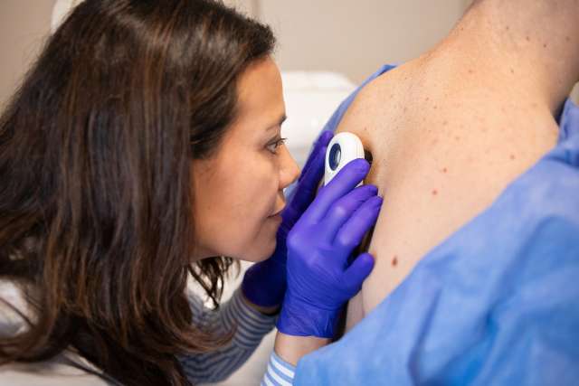 Dermatologist examines patient's skin with a handheld magnifier.