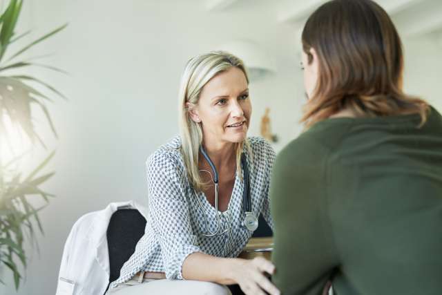 Doctor with stethoscope talking to a patient in a bright office.